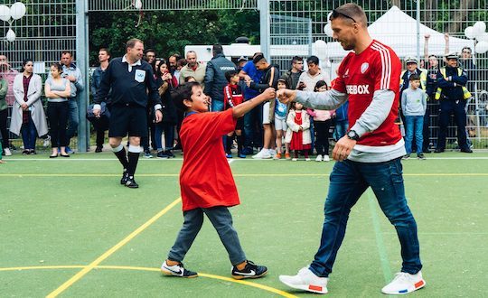 Lukas Podolski macht einen Handschlag mit Jungen bei einem Event der Lukas Podolski Stiftung
